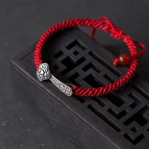 Red string Ruyi luck bracelet with carved silver ornament and red agate bead on Chinese wooden decor, top view