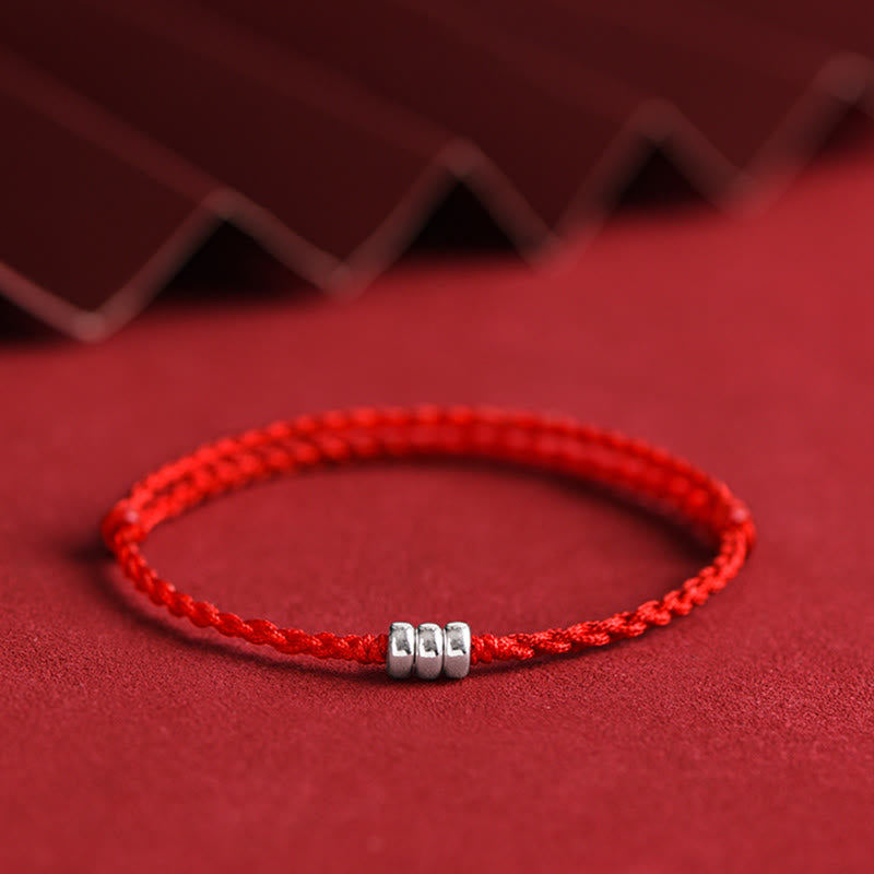 Braided red string bracelet featuring handmade silver bead charms on fabric background