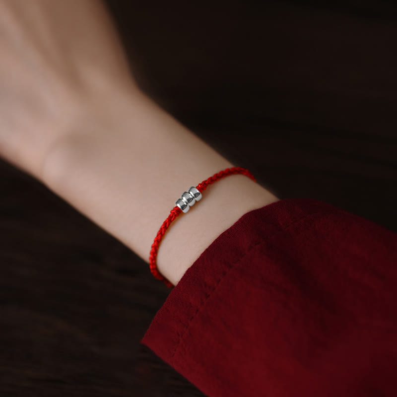Red string bracelet with silver beads worn on wrist, side close-up view showing wear effect
