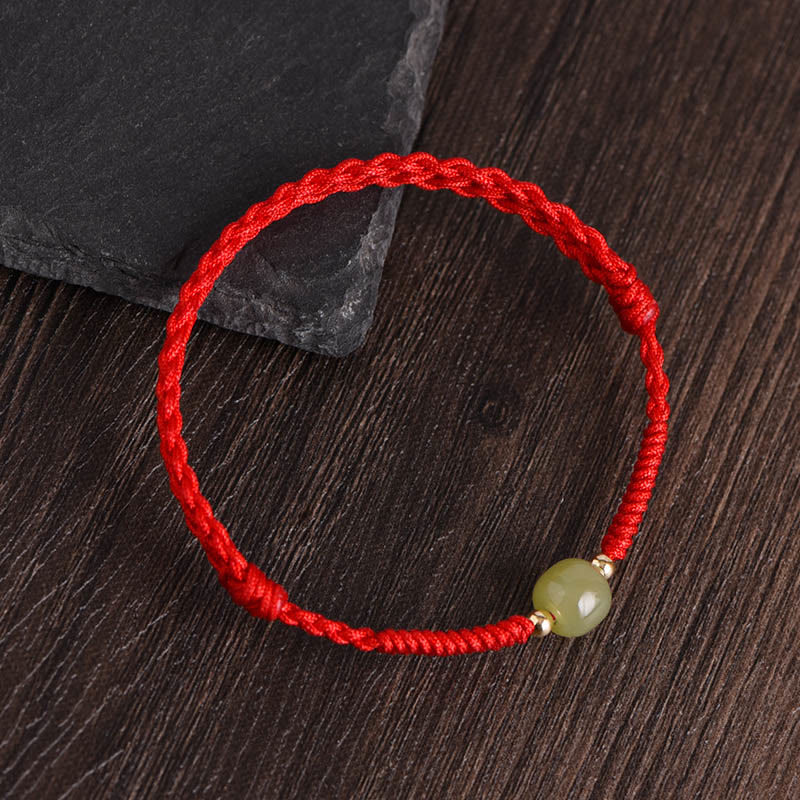 Red braided jade gold bead bracelet side view dark wood background