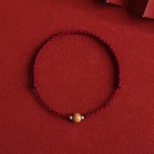 Red string peach wood bracelet with wooden bead - top view flat lay on red fabric background