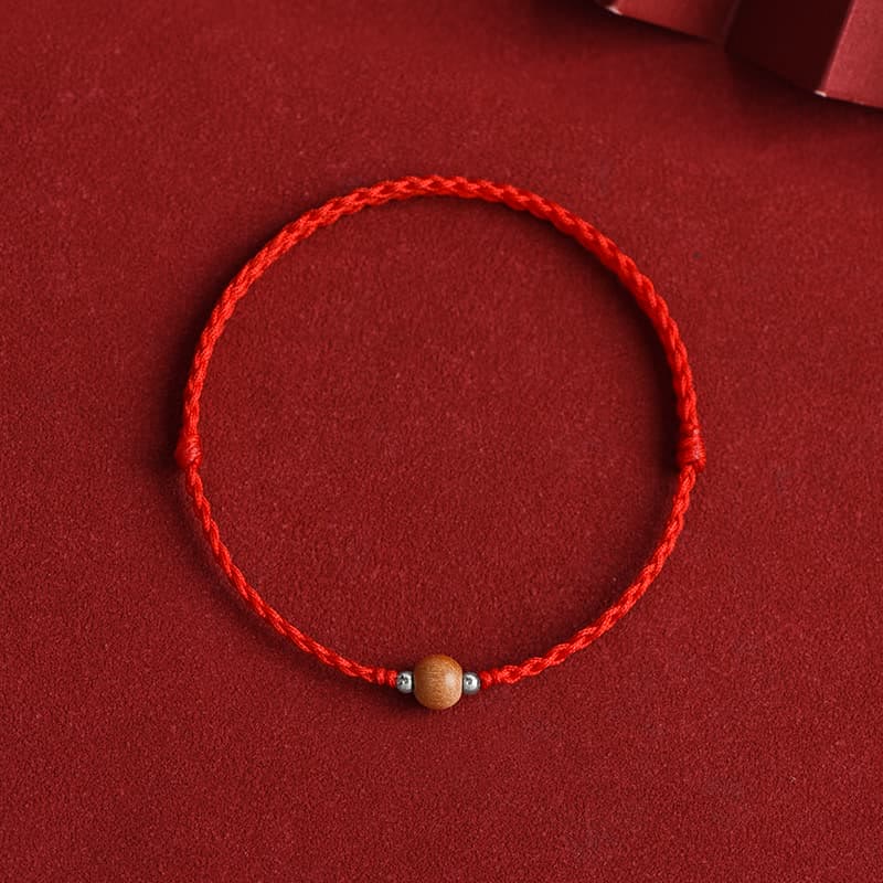 Bright red braided peach wood luck bracelet with light brown bead - flat lay overhead