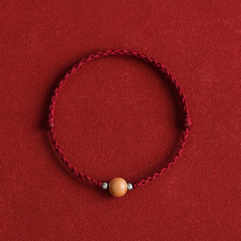 Peach wood bead braided red string bracelet - overhead shot showing wood grain detail