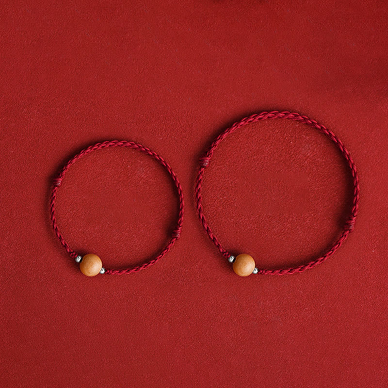 Two matching red braided peach wood luck bracelets flat lay on red fabric