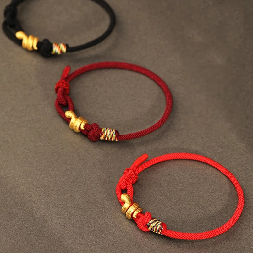 red string bracelet gold snake charm next to 2025 new year decoration