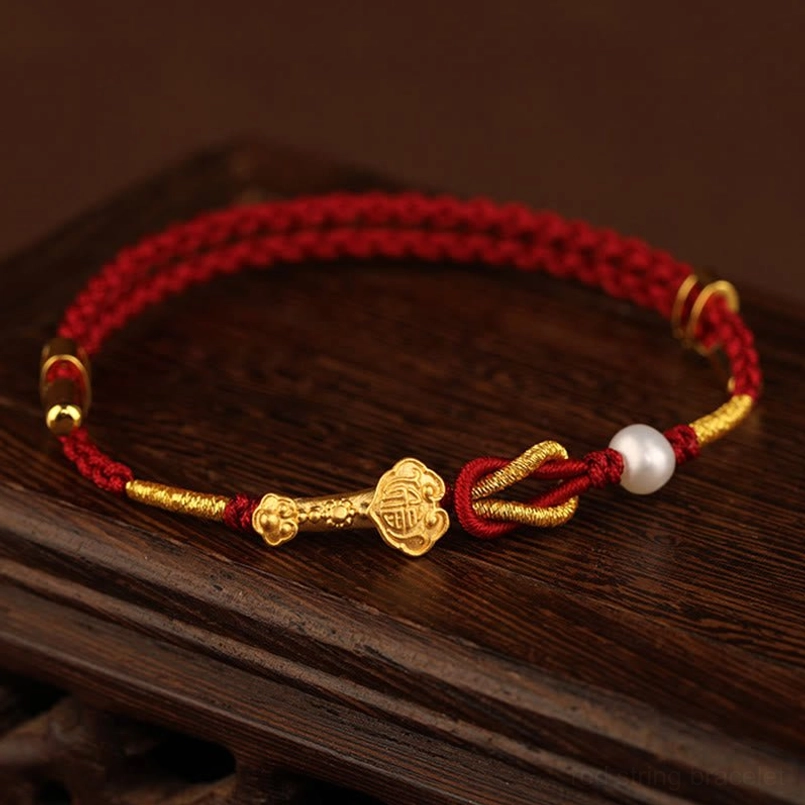 Ruyi Fu character red string bracelet overhead view with gold charm and pearl on wooden background