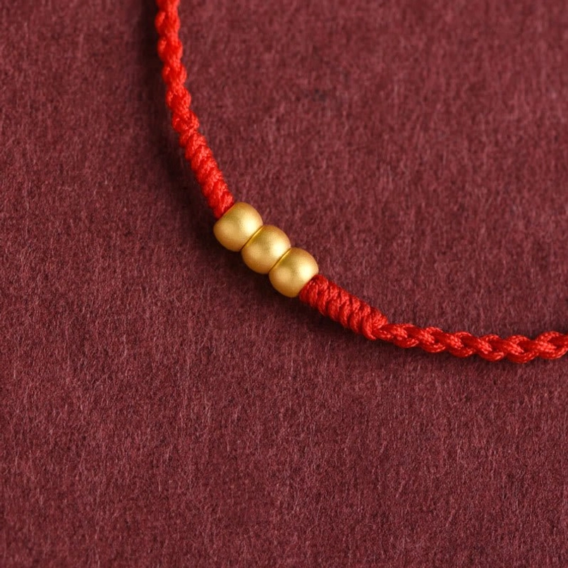 Close up of 3 matte 999 gold beads on red luck string bracelet