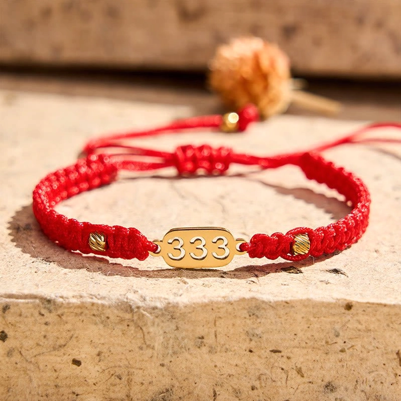 333 angel number red braided bracelet with gold tag wooden background