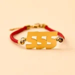 555 angel number red string bracelet with golden titanium steel charm on beige background flat lay