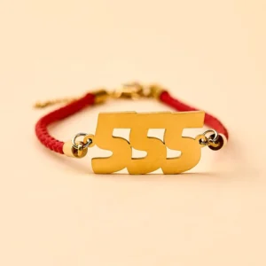 555 angel number red string bracelet with golden titanium steel charm on beige background flat lay