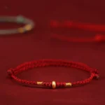 999 gold lucky bead red string bracelet side close-up with wine red background