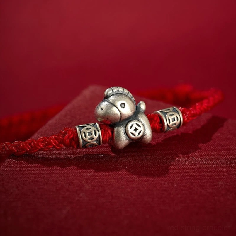 Close up of engraved 999 sterling silver horse charm on red braided bracelet