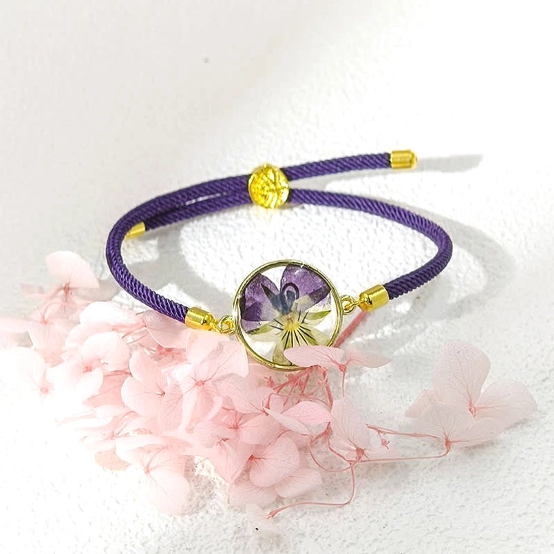 Purple adjustable birth flower red string bracelet with resin-encased pansy pendant - flat lay view