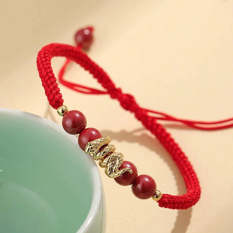 Side view of adjustable knot cinnabar snake red string bracelet next to ceramic cup