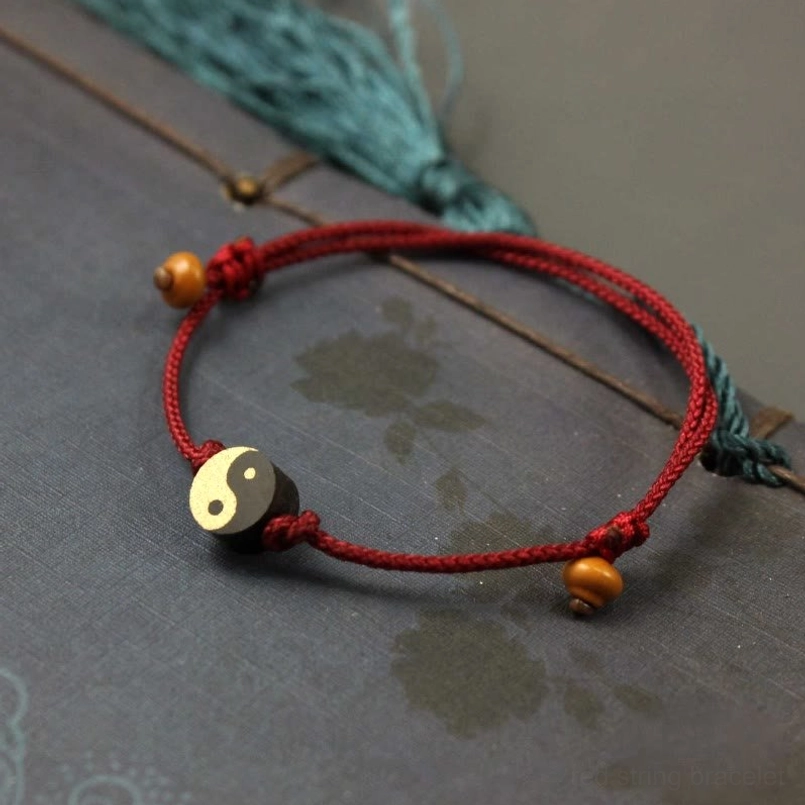Yin Yang red bracelet with adjustable knot on patterned fabric background