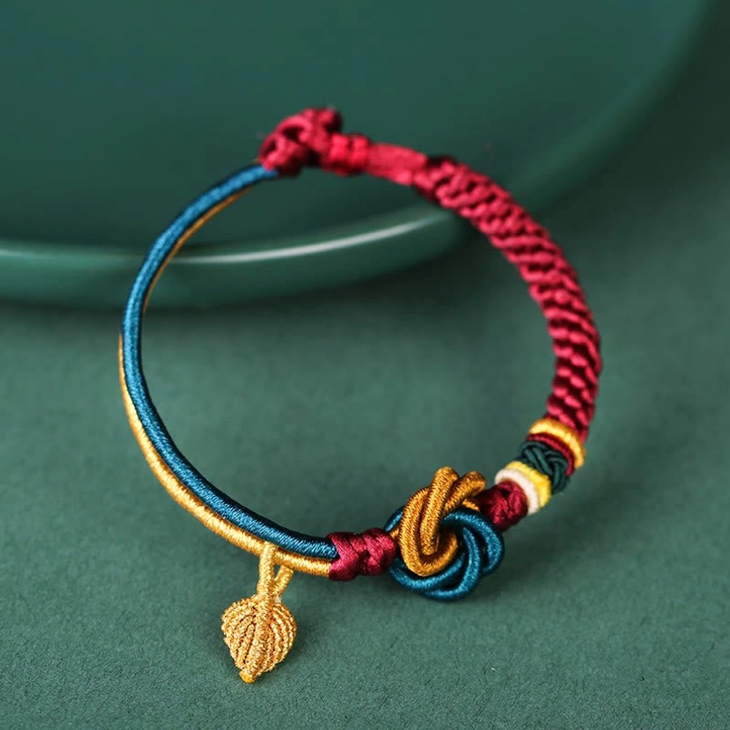Adjustable braided luck bracelet flat lay on dark green plate with knot and leaf charm