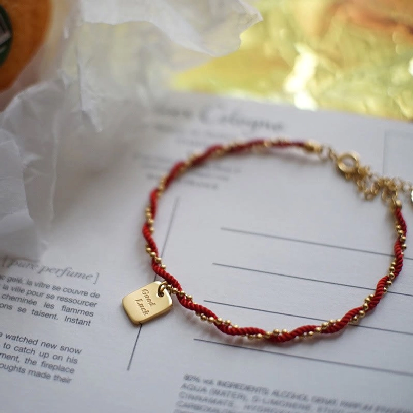 Adjustable red cord bracelet side view with gold extender chain on perfume paper