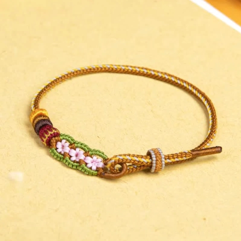 Lucky red string bracelet with pink flower weave, silver rings and colored bead accents on beige background
