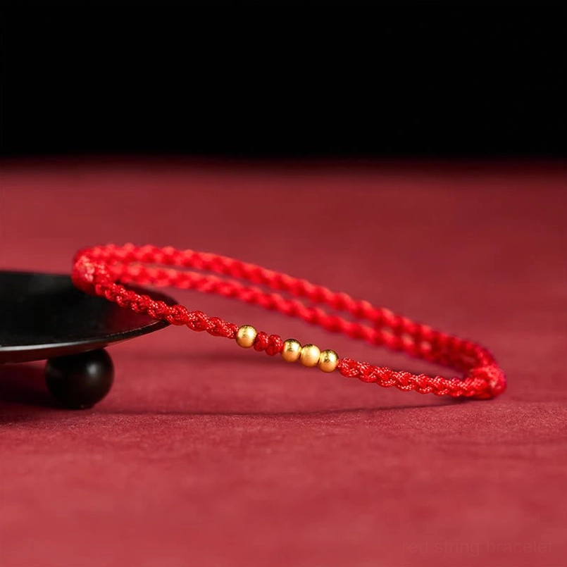 Adjustable red string gold bead bracelet oblique side view on red background