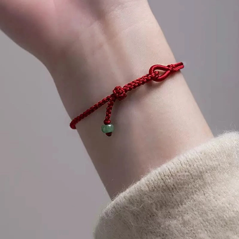 Side view of adjustable red string jade bracelet worn on casual wrist