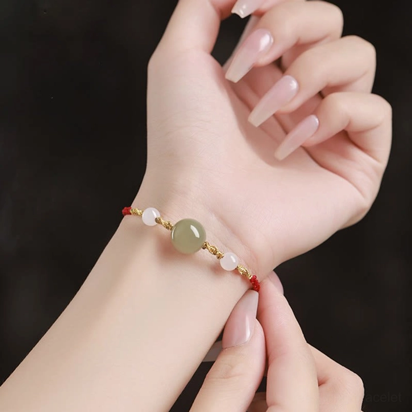 Hands adjusting red string bracelet tightness, close-up detail view