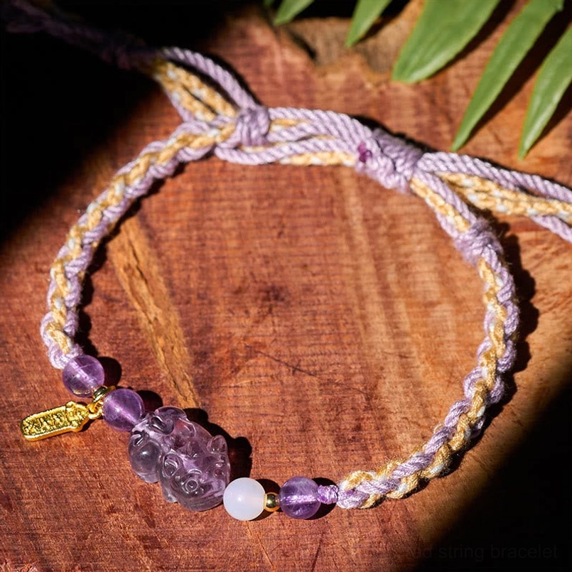 Side flat lay of amethyst Pixiu red string bracelet with green foliage decoration