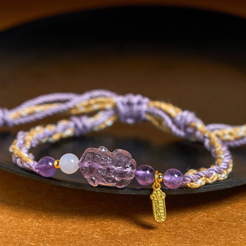 Close up of braided purple tan red string amethyst Pixiu bracelet on dark ceramic plate