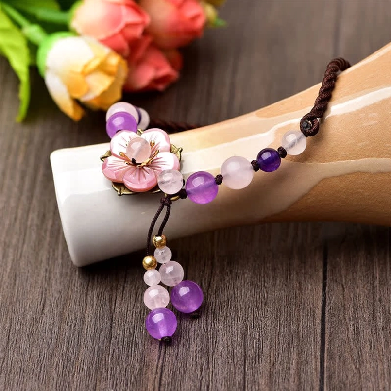 Close-up side angle of amethyst beads and rose quartz flower charm with tassel on decorative background