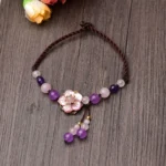 Amethyst rose quartz crystal flower anklet flat lay with braided cord and tassel charm on wooden surface