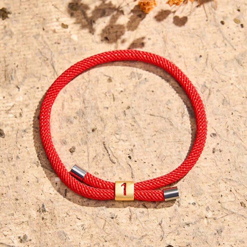 Angel number 1 red string bracelet flatlay with textured stone background