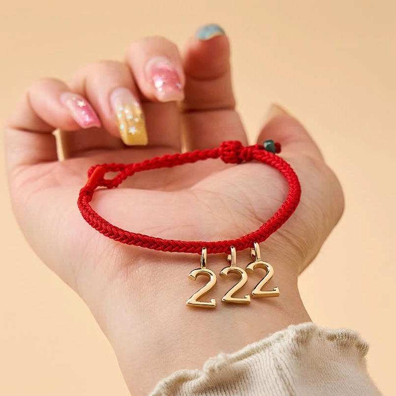 Angel number red string jade bracelet worn on wrist, showing braided red rope with gold number charm and jade accent in everyday wear