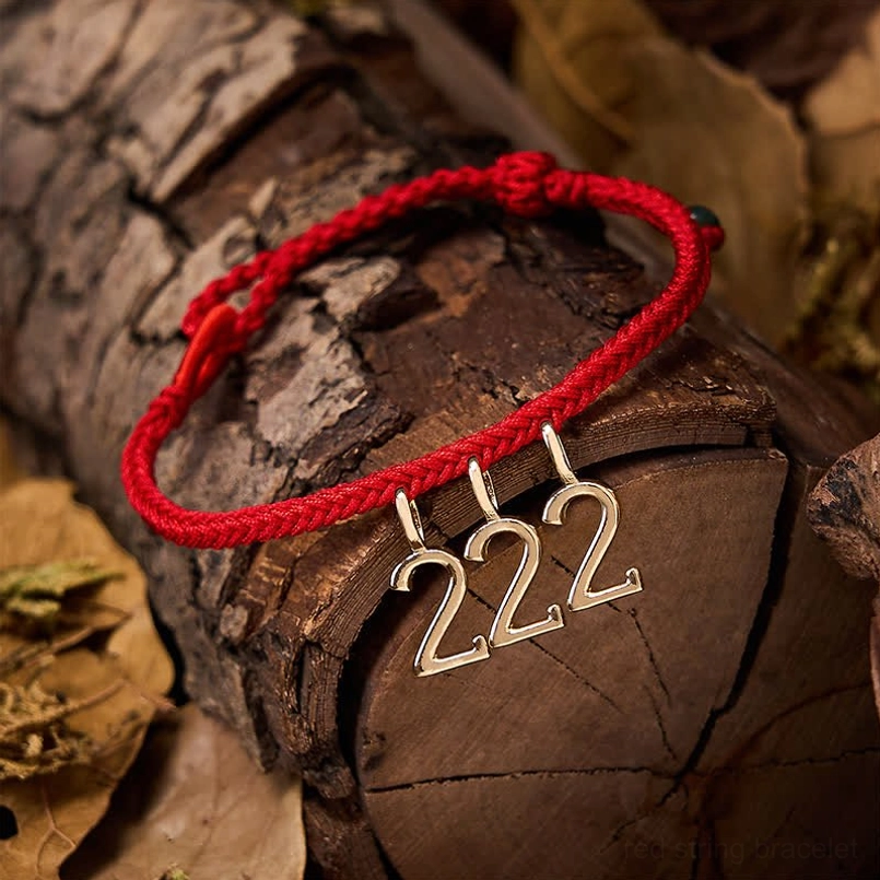 Angel number red string jade bracelet displayed on natural wood, showing braided red cord with gold pendant and jade accents