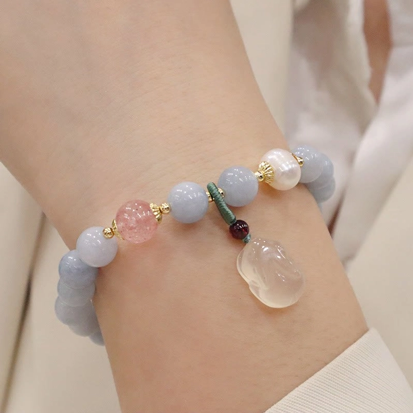 Light blue aquamarine beaded bracelet with gold peace buckle charm and accent beads, side view on wrist