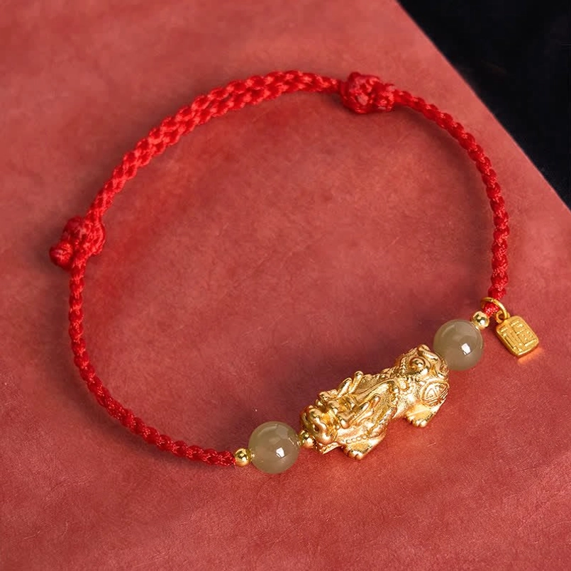 Simple red braided Pi Xiu jade bead bracelet top view on dark red fabric background