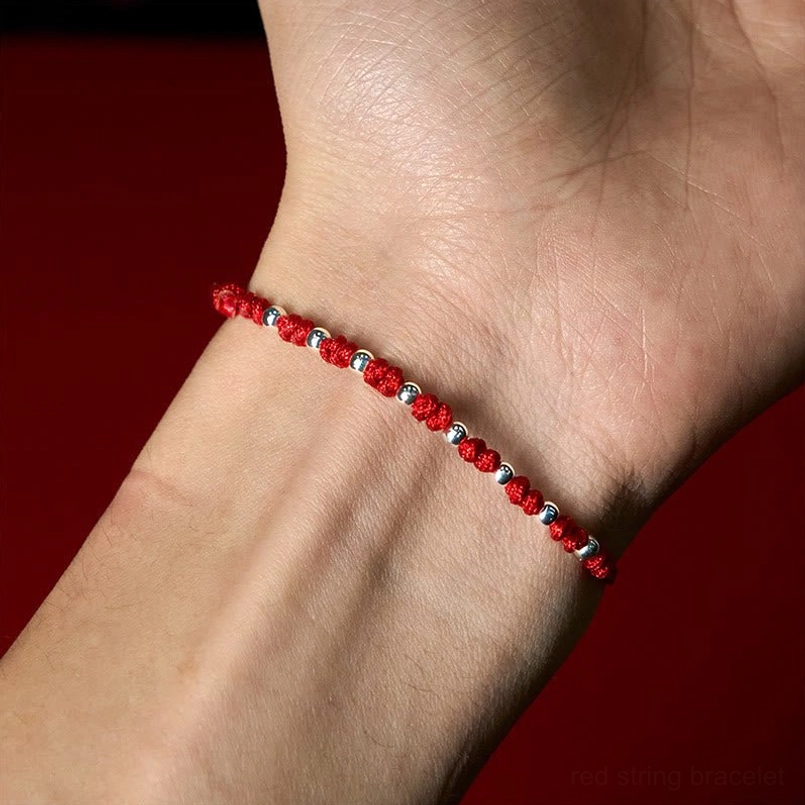 Red string luck bracelet with silver beads displayed on red velvet showing authentic handmade craftsmanship
