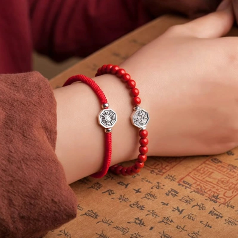 Minimalist bagua charm red cord bracelet on wrist with brown sleeve