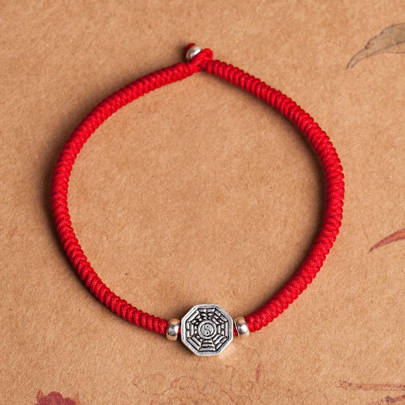 Handcrafted yin yang bagua red woven rope bracelet with silver pendant flat lay
