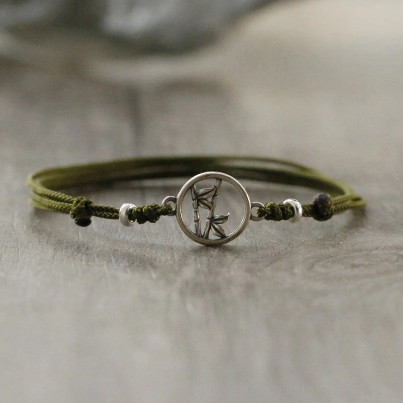 Sterling silver bamboo red string bracelet with braided olive cord and decorative end knots on wood surface