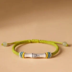Yellow-green bamboo red string bracelet with 999 sterling silver charm and jade adjusters, flat lay view
