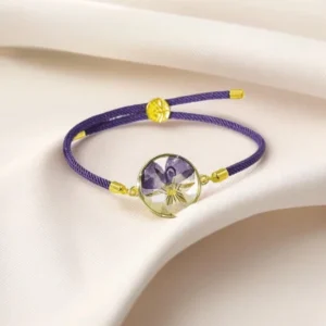 Purple braided rope birth flower bracelet with gold-toned resin pansy charm - side overhead view