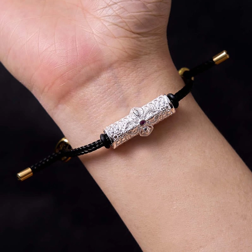 Red string bracelet style with black cord, copper charm, and enamel flower detail