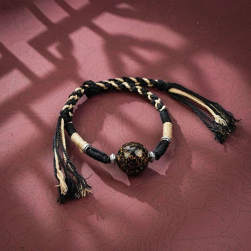 Black braided red string bracelet with dark patterned lacquer bead and frayed tassels