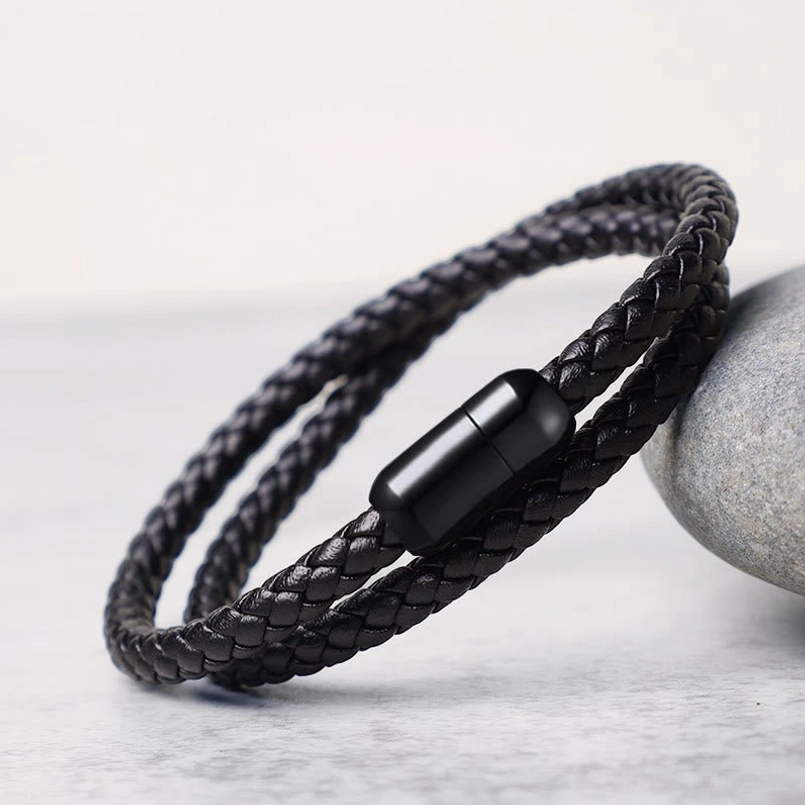 Double-wrap black leather red string bracelet with magnetic buckle, side perspective on textured background