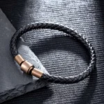 Black braided leather bracelet with bronze magnetic clasp on dark slate texture