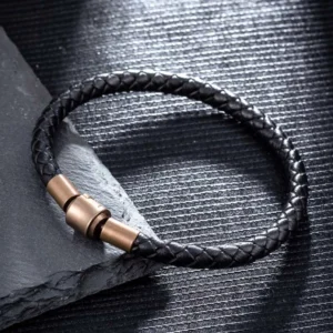 Black braided leather bracelet with bronze magnetic clasp on dark slate texture