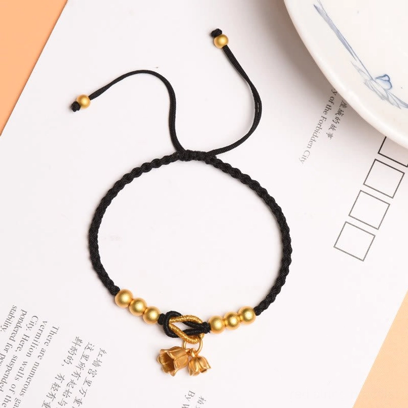 Black adjustable luck bracelet with lily charm and gold beads on styled surface
