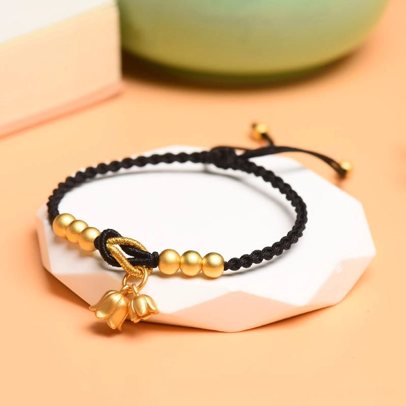 Black woven string bracelet with lily of the valley charm and matte gold details