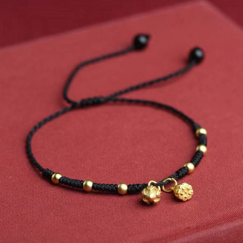 Black lotus pod charm anklet with dual gold lotus pendants and sliding knot on red background