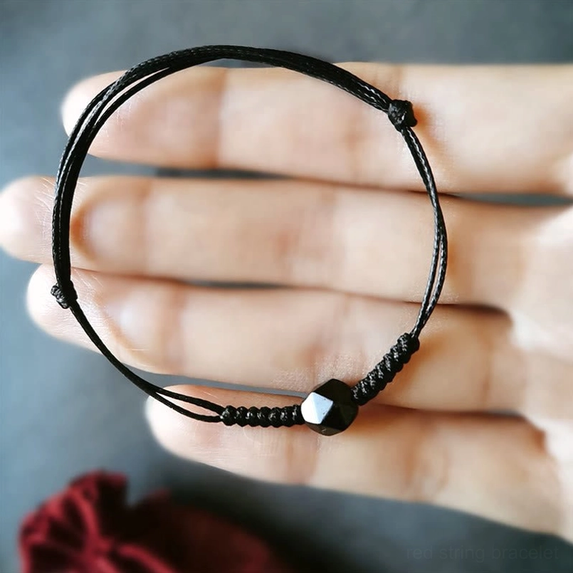 Adjustable black obsidian bracelet held in palm showing double thin braided cords and faceted bead
