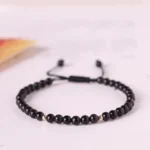 Black obsidian 4mm beaded red string bracelet with gold accents, flat lay view on light surface